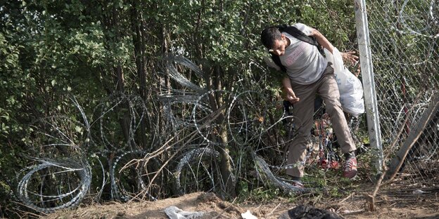 EIn Flüchtlinge klettert im Herst 2015 durch ein Loch in Zaun von Serbien nach Ungarn