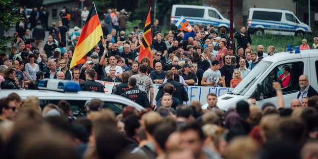 Viele Menschen mit einer Deutschlandfahne und der Flagge Deutscher Widerstand 20. Juli. Davor Polizeikräfte Viele Menschen mit einer Deutschlandfahne und der Flagge Deutscher Widerstand 20. Juli. Davor Polizeikräfte