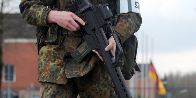 Ein Soldat hält ein Gewehr in der Hand, hinter ihm weht eine Deutschlandfahne Ein Soldat hält ein Gewehr in der Hand, hinter ihm weht eine Deutschlandfahne
