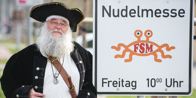 Ein als Pirat verkleideter Mann steht neben einem Schild mit der Aufschrift "Nudelmesse" Ein als Pirat verkleideter Mann steht neben einem Schild mit der Aufschrift "Nudelmesse"