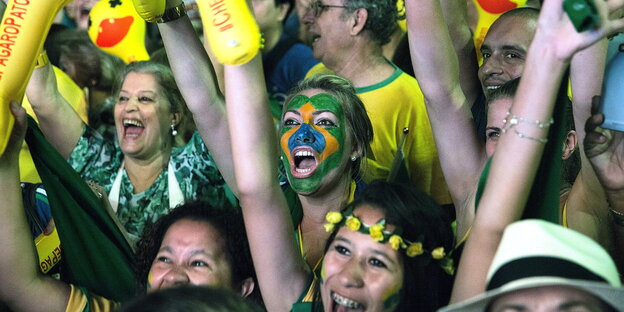 Menschen sind in den Farben der brasilianischen Flagge gekleidet und feiern, eine Frau ist in grün-gelb geschminkt Menschen sind in den Farben der brasilianischen Flagge gekleidet und feiern, eine Frau ist in grün-gelb geschminkt