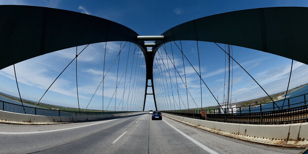 Ein Auto fährt unter den mächtigen Bögen der Fehmarnsundbrücke.