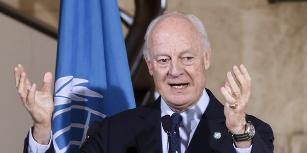 Staffan de Mistura steht hinter einem Mikrofon und hebt die Hände Staffan de Mistura steht hinter einem Mikrofon und hebt die Hände