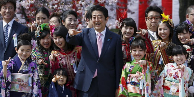Japans Premier Shinzo Abe und als Geishas verkleidete Mädchen zeigen beim Kirschblütenfest in die Kamera Japans Premier Shinzo Abe und als Geishas verkleidete Mädchen zeigen beim Kirschblütenfest in die Kamera