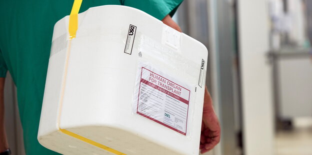 Ein Mensch im grünen Kittel trägt einen Behälter zum Transport von Organen Ein Mensch im grünen Kittel trägt einen Behälter zum Transport von Organen