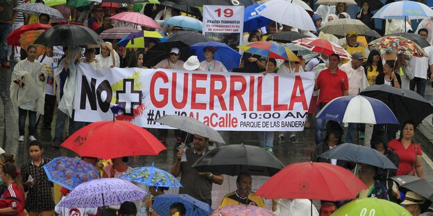 Menschen tragen bunte Regenschirme und ein Transparent gegen die Farc Menschen tragen bunte Regenschirme und ein Transparent gegen die Farc