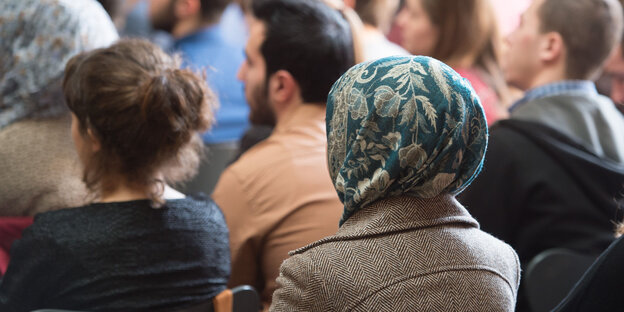 Menschen mit und ohne Kopftücher sitzen zusammen im Publikum Menschen mit und ohne Kopftücher sitzen zusammen im Publikum