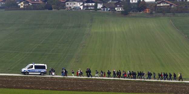 Auf einem Feldweg folg eine Gruppe Menschen einem Polizeifahrzeug