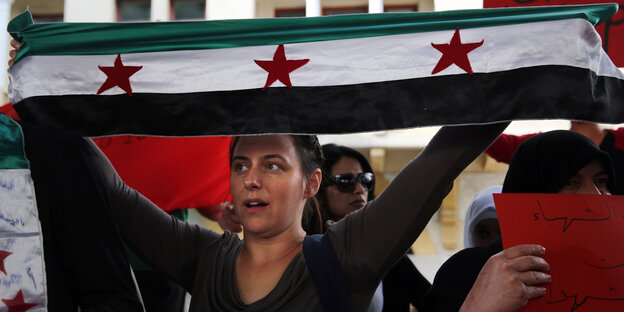 Eine Frau hält die Fahne der syrischen Revolution hoch Eine Frau hält die Fahne der syrischen Revolution hoch