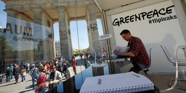Mann sitzt im Greenpeace-Glaskasten vor dem Brandenburger Tor und nimmt Einblick in die geleakten Papers
