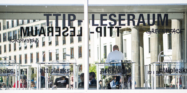 Ein Mensch sitzt in einem gläsernen Raum mit der Aufschrift "TTIP-Leseraum" Ein Mensch sitzt in einem gläsernen Raum mit der Aufschrift "TTIP-Leseraum"
