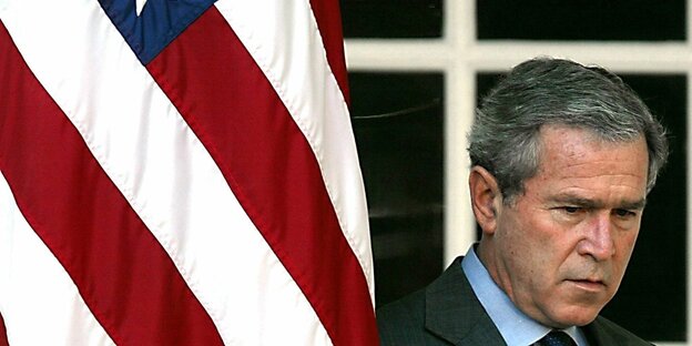 Ein Mann schaut auf den Boden, neben ihm ist eine US-Flagge Ein Mann schaut auf den Boden, neben ihm ist eine US-Flagge