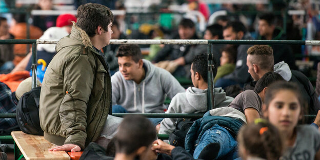 Menschen sitzen auf Bänken in einer Halle Menschen sitzen auf Bänken in einer Halle