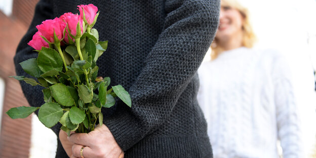 Ein Mensch hält einen Blumenstrauß hinter dem Rücken Ein Mensch hält einen Blumenstrauß hinter dem Rücken