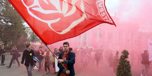 Fahnenträger vor Demo in rötlichen Rauchschwaden