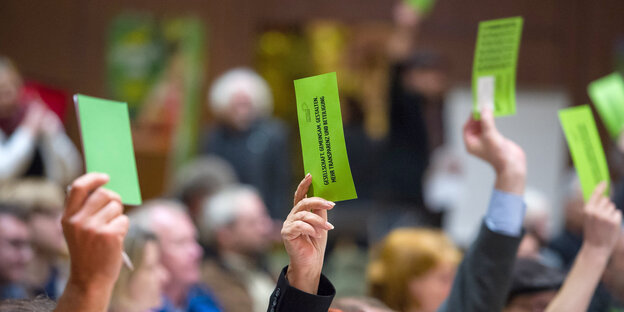 Menschen heben ihre Arme, in den Händen halten sie grüne Zettel Menschen heben ihre Arme, in den Händen halten sie grüne Zettel