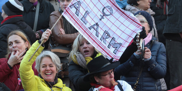 Eine Frau schwenkt eine Fahne, auf der das Frauensymbol und die Aufschrift „Alarm“ zu sehen sind