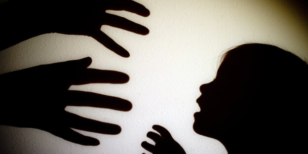 Schatten an der Wand: Zwei Hände greifen nach einem Kind Schatten an der Wand: Zwei Hände greifen nach einem Kind