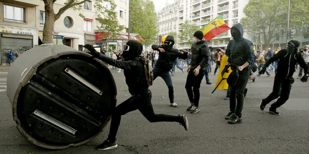 Schwarz gekleidet und vermummte Demonstranten rollen einen Altglascontainer die Straße entlang Schwarz gekleidet und vermummte Demonstranten rollen einen Altglascontainer die Straße entlang