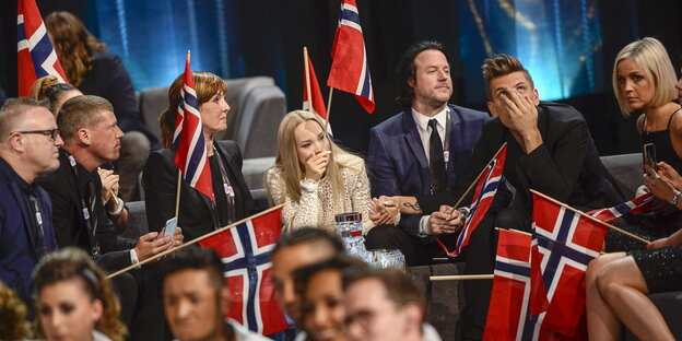 Eine Gruppe von Menschen hält norwegische Flaggen in den Händen und hat schockierte Gesichtausdrücke Eine Gruppe von Menschen hält norwegische Flaggen in den Händen und hat schockierte Gesichtausdrücke