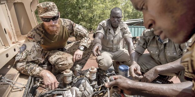 Ein Bundeswehr-Soldat hilft einem malischen Soldaten bei der Reparatur eines Autos Ein Bundeswehr-Soldat hilft einem malischen Soldaten bei der Reparatur eines Autos