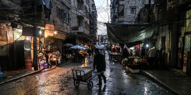 Ein Mann schiebt einen Handwagen durch eine Einkaufsstraße in Aleppo. Es regnet stark Ein Mann schiebt einen Handwagen durch eine Einkaufsstraße in Aleppo. Es regnet stark