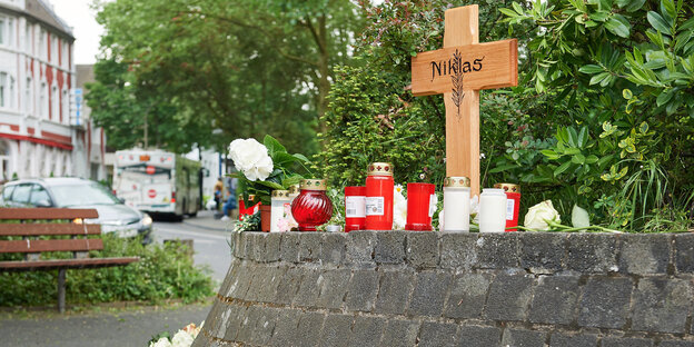 ein Kreuz mit der Aufschrift "Niklas" und Kerzen, im Hintergrund eine Straßenszene ein Kreuz mit der Aufschrift "Niklas" und Kerzen, im Hintergrund eine Straßenszene