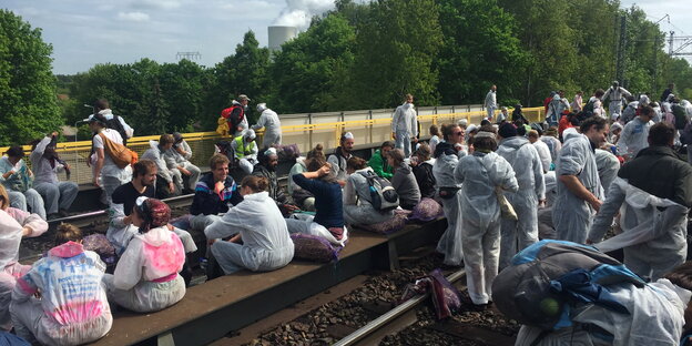 Menschen in Schutzanzügen sitzen auf Bahnschienen Menschen in Schutzanzügen sitzen auf Bahnschienen