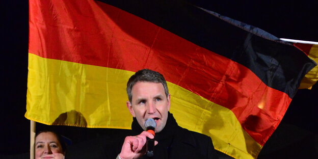 ein Mann mit Mikrofon vor einer Deutschlandfahne ein Mann mit Mikrofon vor einer Deutschlandfahne