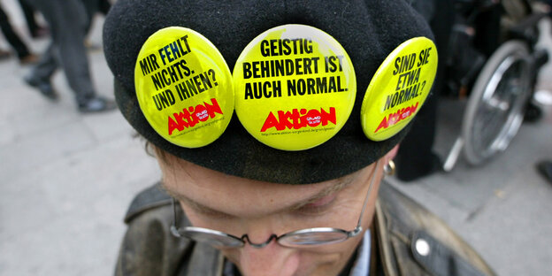 Ein Mann, der Sticker mit der Aufschrift "Geistig behindert ist auch normal" an seiner Mütze trägt Ein Mann, der Sticker mit der Aufschrift "Geistig behindert ist auch normal" an seiner Mütze trägt