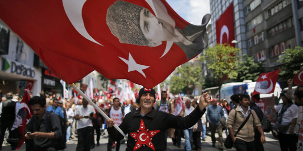 Ein Mann trägt auf einer Demo eine türkische Fahne mit dem Konterfei von Kemal Atatürk durch die Straße Ein Mann trägt auf einer Demo eine türkische Fahne mit dem Konterfei von Kemal Atatürk durch die Straße
