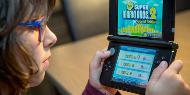 Ein Mädchen mit Brille spielt auf einem Gameboy das Spiel SuperMario Ein Mädchen mit Brille spielt auf einem Gameboy das Spiel SuperMario