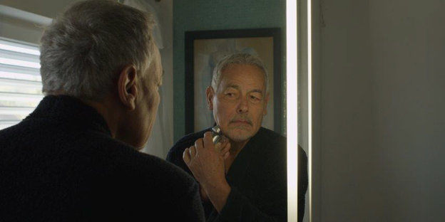 Ein älterer Mann blickt in einen Spiegel und rasiert sich