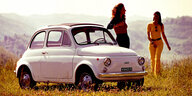 Eine junge Frau lehnt sich lässig an einen alten, weißen Fiat 500. Eine weitere kommt ihr entgegen