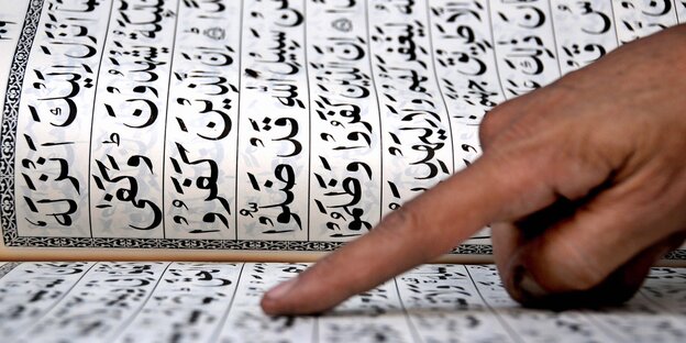 Eine Hand liegt auf einer Seite eines aufgeschlagenen Korans Eine Hand liegt auf einer Seite eines aufgeschlagenen Korans