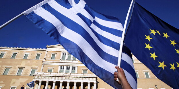Die griechische Flagge und die EU-Flagge werden vor einem Gebäude geschwenkt Die griechische Flagge und die EU-Flagge werden vor einem Gebäude geschwenkt