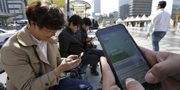 Männer sitzen auf einem öffentlichen Platz und tippen in ihre Smartphones Männer sitzen auf einem öffentlichen Platz und tippen in ihre Smartphones