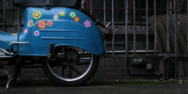 Ein blauer Motorroller mit Prilblumen beklebt steht an einem Zaun Ein blauer Motorroller mit Prilblumen beklebt steht an einem Zaun