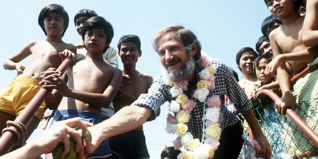 Rupert Neudeck mit einer Blumenkette, umgeben von Kindern