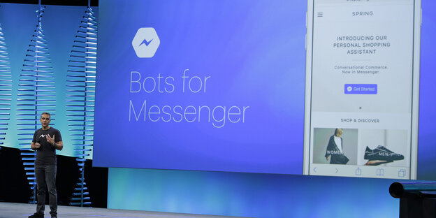 David Marcus steht vor einem blauen digitalen Großdisplay, auf dem „Bots for Messenger“ steht David Marcus steht vor einem blauen digitalen Großdisplay, auf dem „Bots for Messenger“ steht