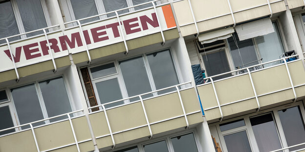 Vorderansicht eines Mehrfamilienhauses mit grauen Balkonen und einem Schild „Vermieten“ Vorderansicht eines Mehrfamilienhauses mit grauen Balkonen und einem Schild „Vermieten“