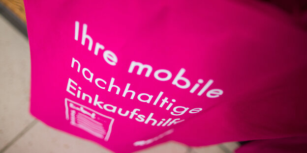 Auf einem pinkfarbenen Baumwollbeutel steht in weiß „Ihre mobile nachhaltige Einkaufshilfe“ Auf einem pinkfarbenen Baumwollbeutel steht in weiß „Ihre mobile nachhaltige Einkaufshilfe“
