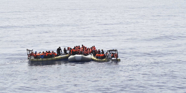 Auf dem Meer schwimmen mehrere Schlauchboote, in denen Menschen mit Rettungswesten stehen Auf dem Meer schwimmen mehrere Schlauchboote, in denen Menschen mit Rettungswesten stehen