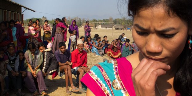 Die Protagonistin Urmila Chaudhary in einem nepalesischen Dorf, im Hintergrund sitzen DorfbewohnerInnen. Die Protagonistin Urmila Chaudhary in einem nepalesischen Dorf, im Hintergrund sitzen DorfbewohnerInnen.
