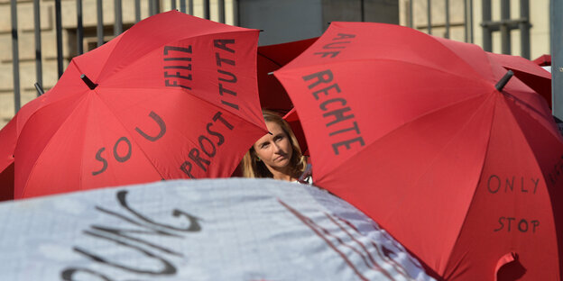 Ein Gesicht zwischen roten und weißen Regenschirmen, auf denen „Prostitution“ und „Rechte“ steht