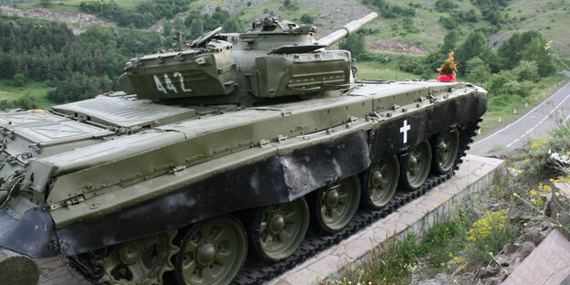 Ein Panzerdenkmal in einer grünen Landschaft, durch die eine Straße führt Ein Panzerdenkmal in einer grünen Landschaft, durch die eine Straße führt