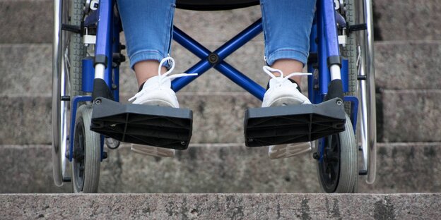 Schuhe einer Frau im Rollstuhl auf einer Treppe
