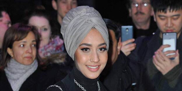 Model Mariah Idrissi mit Turban, im Hintergrund fotografierende Menschen Model Mariah Idrissi mit Turban, im Hintergrund fotografierende Menschen
