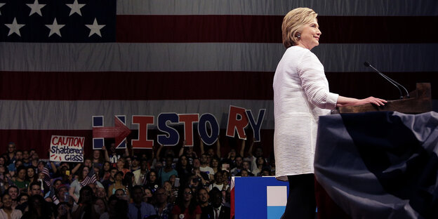 Hillary Clinton steht am Podium, Unstersützer halten Poster in die Höhe mit der Aufschrift "History" Hillary Clinton steht am Podium, Unstersützer halten Poster in die Höhe mit der Aufschrift "History"