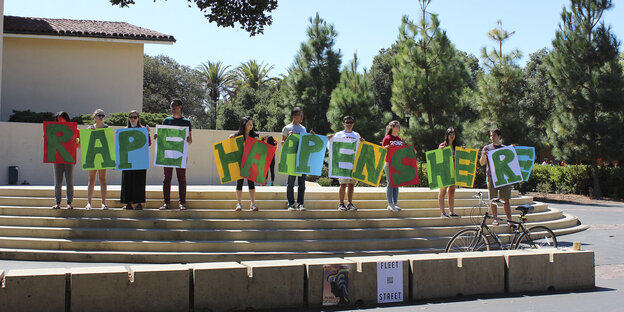 Student_innen halten Buchstaben hoch, die den Satz „Rape happens here“ ergeben Student_innen halten Buchstaben hoch, die den Satz „Rape happens here“ ergeben